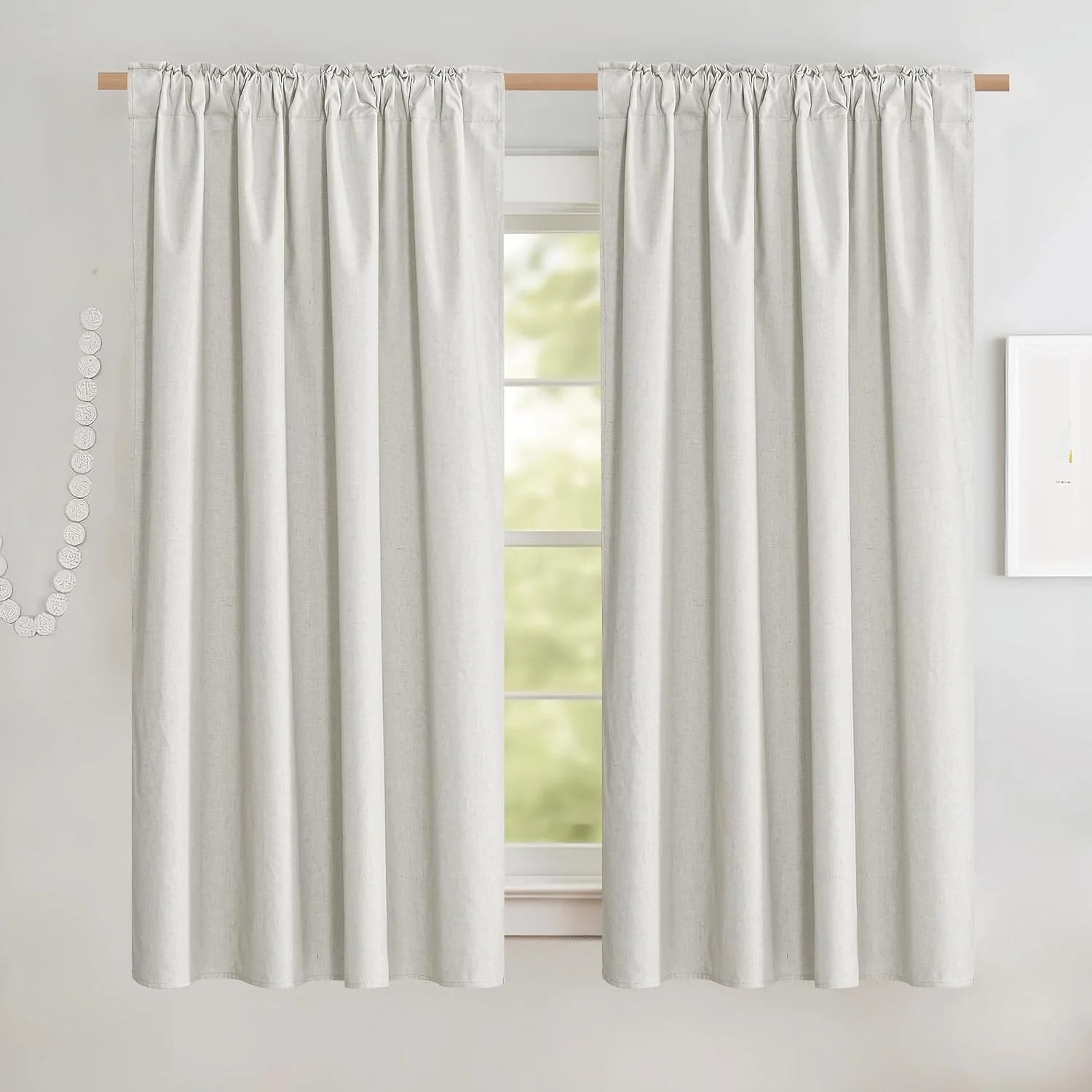Ivory linen-look rod pocket curtains hanging on a wooden rod in a bright room
