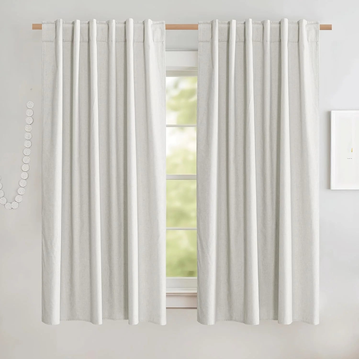 Ivory linen-look rod pocket curtains hanging on a light wood rod in a bright room