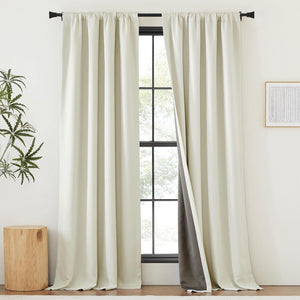 Off-white blackout curtains with a rod pocket hanging on a black rod, revealing dark grey thermal lining.