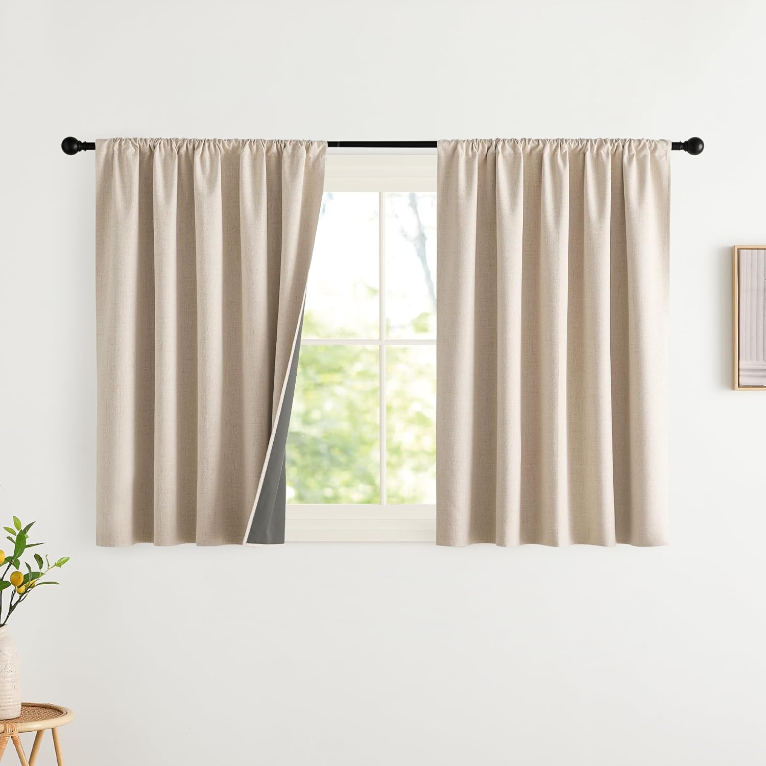 Light beige textured rod pocket curtains with dark grey blackout lining, on black rod.