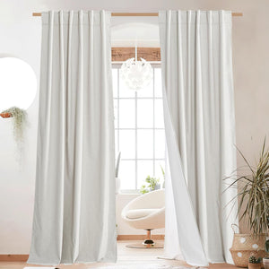 Pair of light beige linen blend curtains with pleated top hanging on a wooden rod in a bright room.