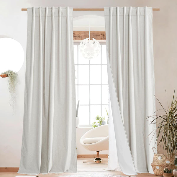 Pair of light beige linen blend curtains with pleated top hanging on a wooden rod in a bright room.
