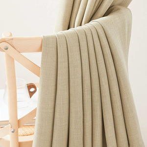 Light beige linen curtain fabric draped on wooden chair, revealing woven texture and soft folds.