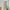 Light beige pleated fabric curtain panel hanging on a silver rod in a doorway, partially revealing shelves and plants.