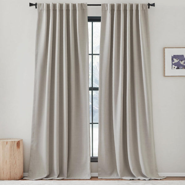 Floor-length light greige textured curtains with tailored pleats hanging on a black rod.