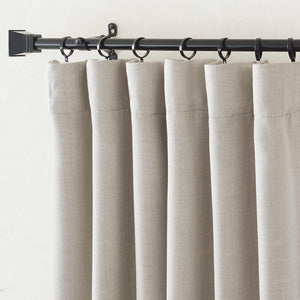 Light beige textured linen-blend curtains hanging on a black rod with ring clips, showcasing soft pleats.