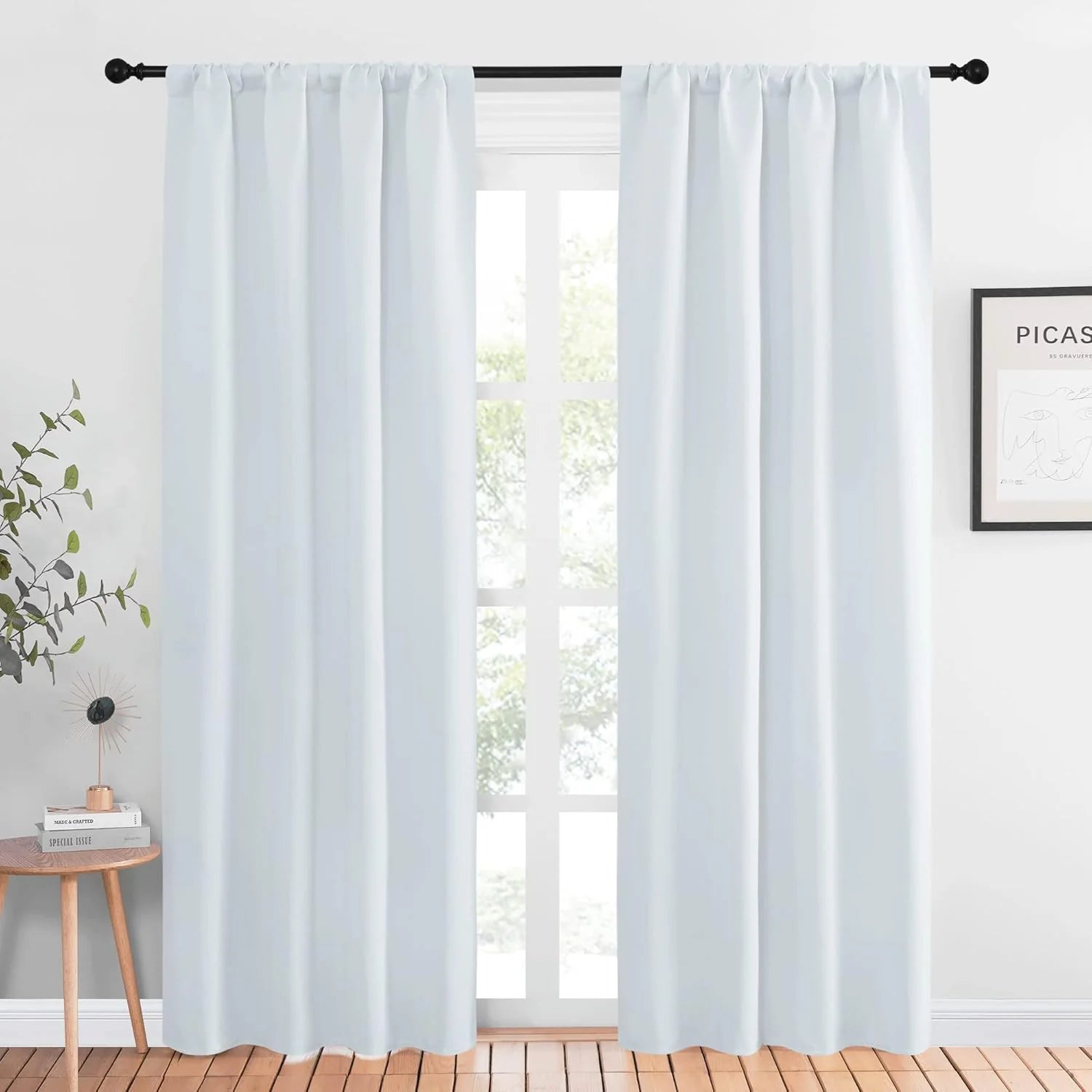 Light blue rod pocket curtains hanging on a black curtain rod in a bright modern room
