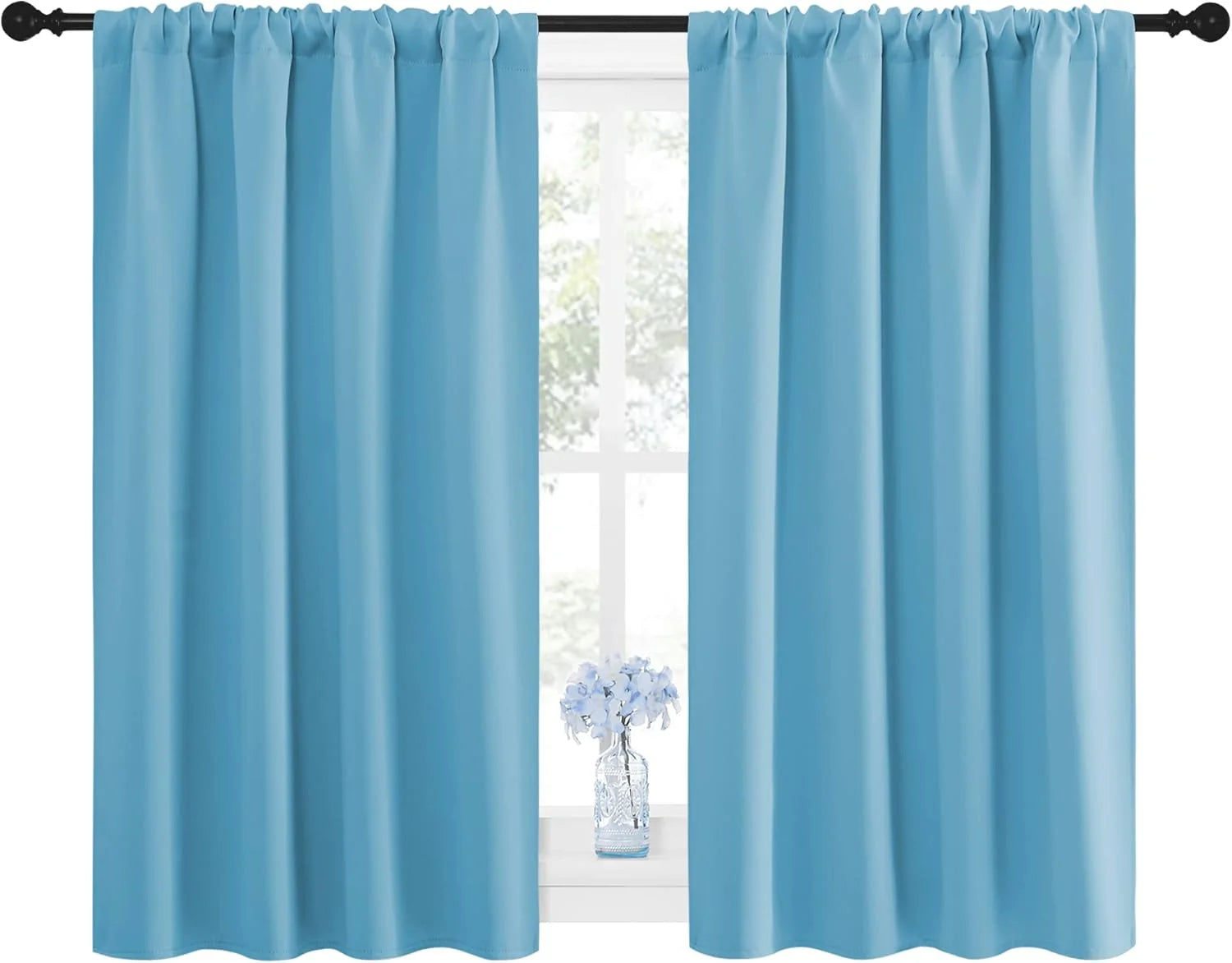 Pair of light blue rod pocket curtain panels on a black rod, covering a window with a small floral vase on the sill.