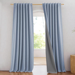 Light blue textured curtains with blackout gray lining hanging from a wooden rod in a bright room.