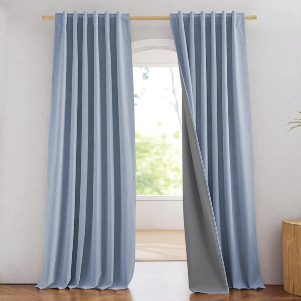 Light blue textured curtains with blackout gray lining hanging from a wooden rod in a bright room.