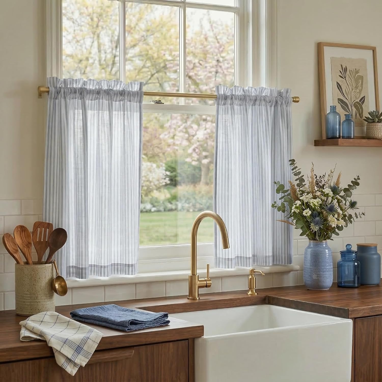 Light blue ticking stripe cafe curtains with ruffled tops on a kitchen window, featuring a brass rod.