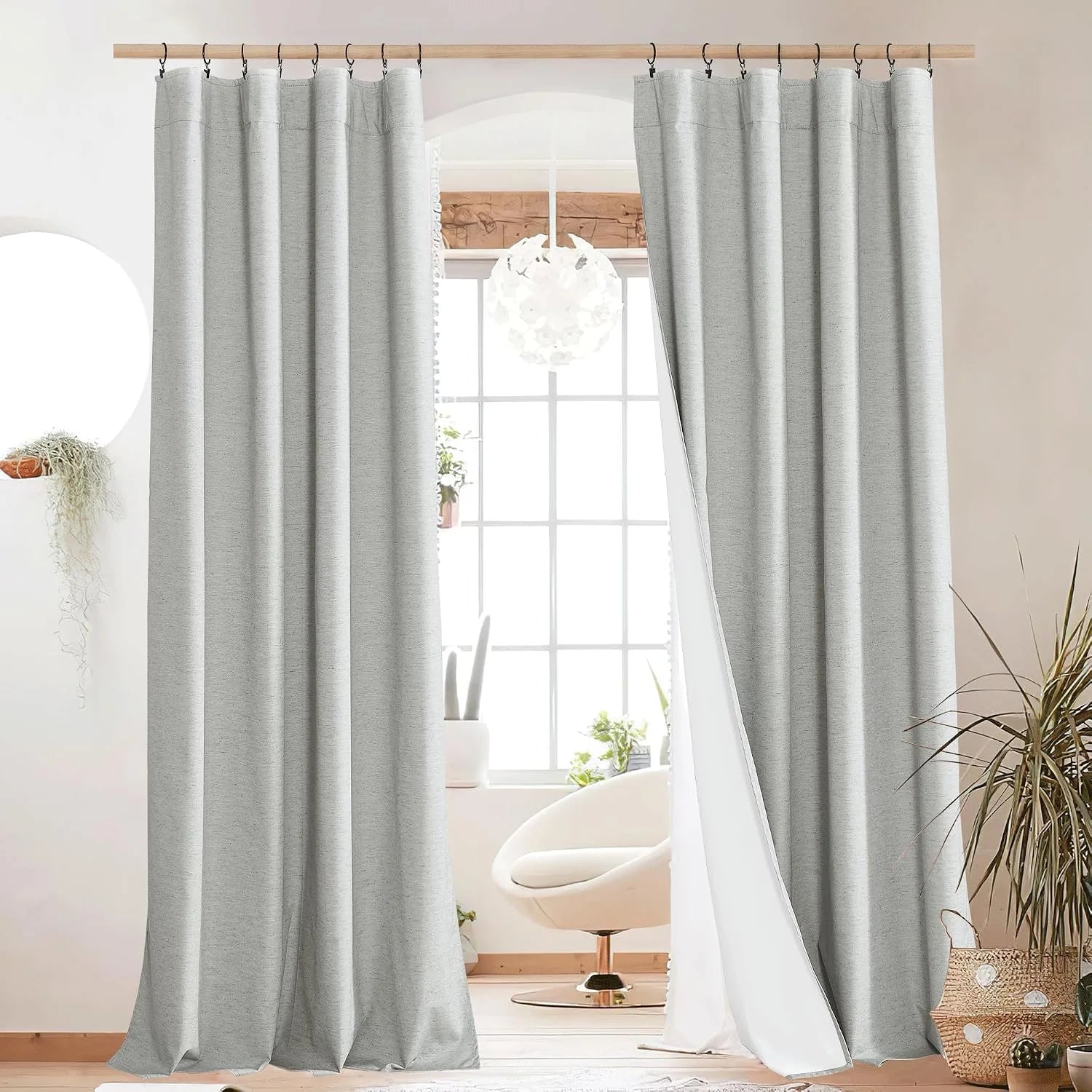 Light gray textured curtain panels on black rings over a bright window