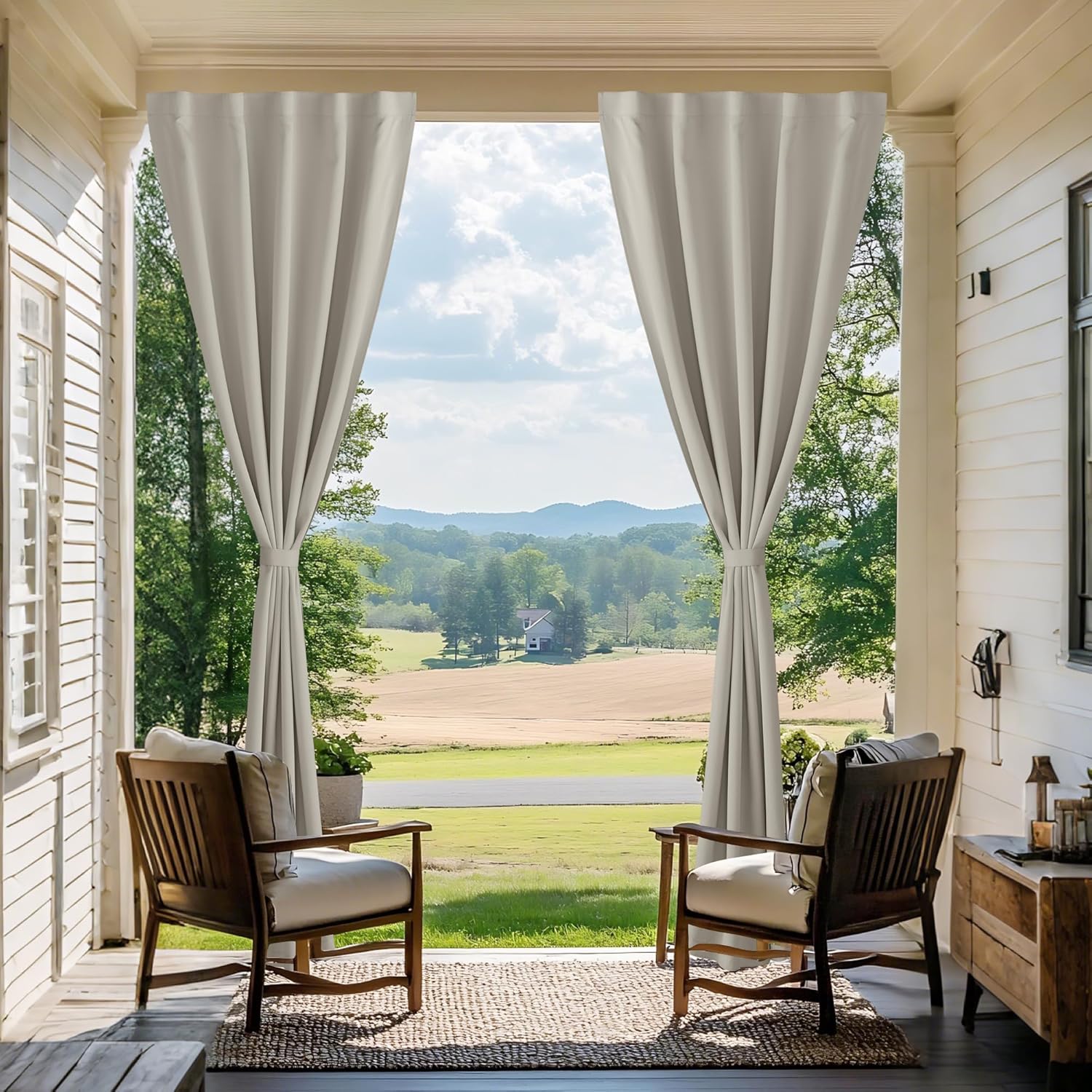 Light gray outdoor curtains with grommet tops, tied back on a porch overlooking a scenic landscape.
