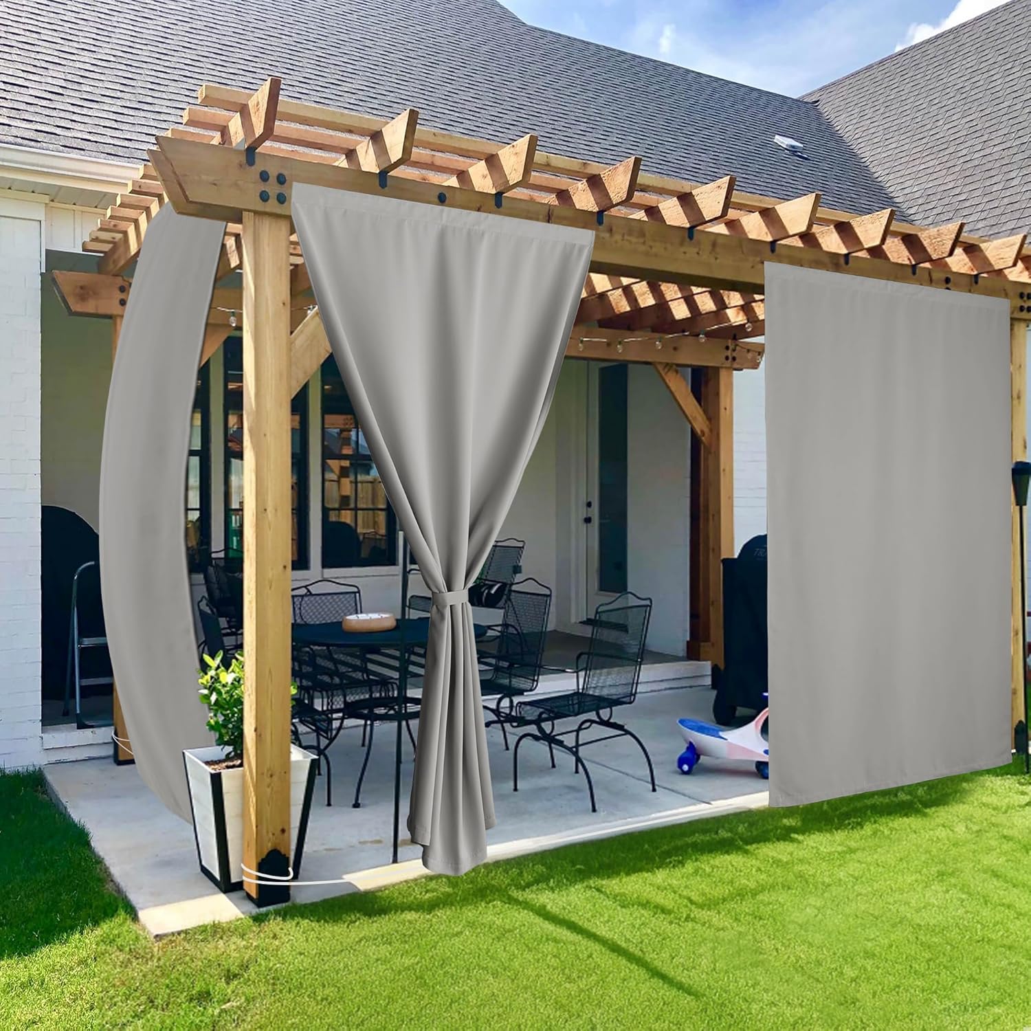 Light gray outdoor curtains hanging on a wooden pergola, one tied back. Provides patio privacy.