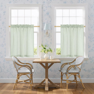 Pair of light green and white striped rod pocket cafe curtains with gathered tops on two windows.