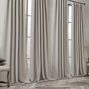 Full length light greige linen pleated drapes cover large windows, pooling on hardwood floors.