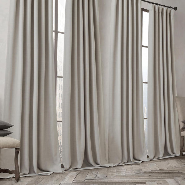 Full length light greige linen pleated drapes cover large windows, pooling on hardwood floors.