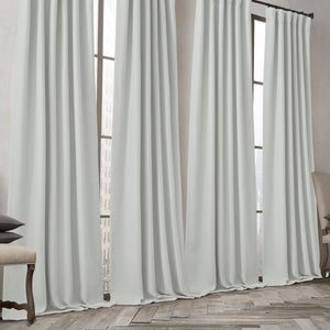 Light grey gathered curtains on a dark rod, covering tall windows and pooling on a wooden floor.