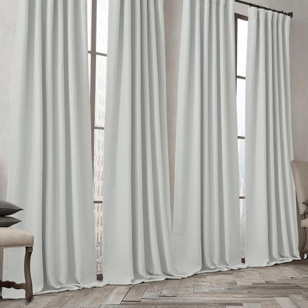 Light grey gathered curtains on a dark rod, covering tall windows and pooling on a wooden floor.