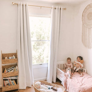 Light grey grommet blackout curtains hanging on a gold rod in a bright nursery with white walls.