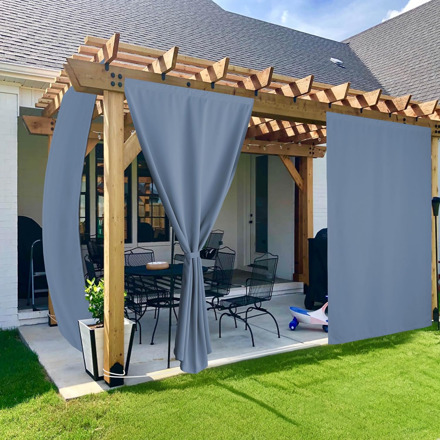 Light grey weatherproof outdoor curtains hanging on a wooden pergola, providing privacy and shade for a patio.