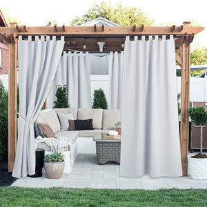 Light grey tab top outdoor curtains hang from a pergola, one tied back, creating a private patio.
