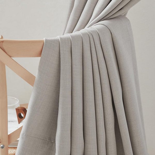 Light grey textured curtain panel with a visible weave, beautifully draped over a light wood chair.