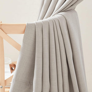Light grey textured curtain panel draped on a wooden chair, showing its woven fabric and soft folds.
