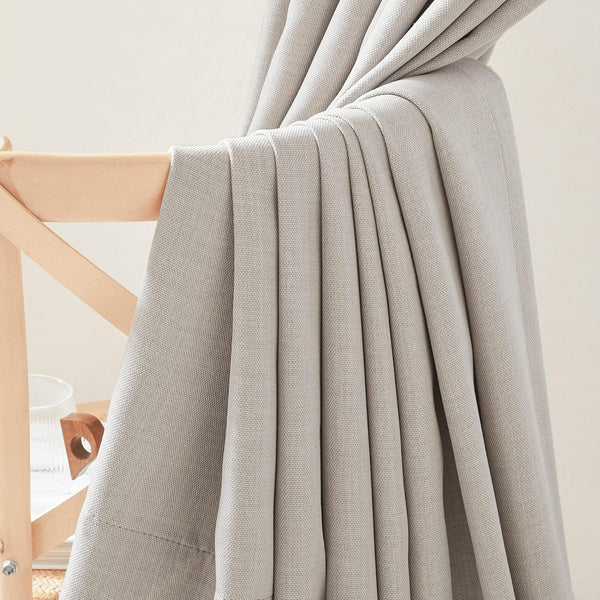 Light grey textured curtain panel draped on a wooden chair, showing its woven fabric and soft folds.