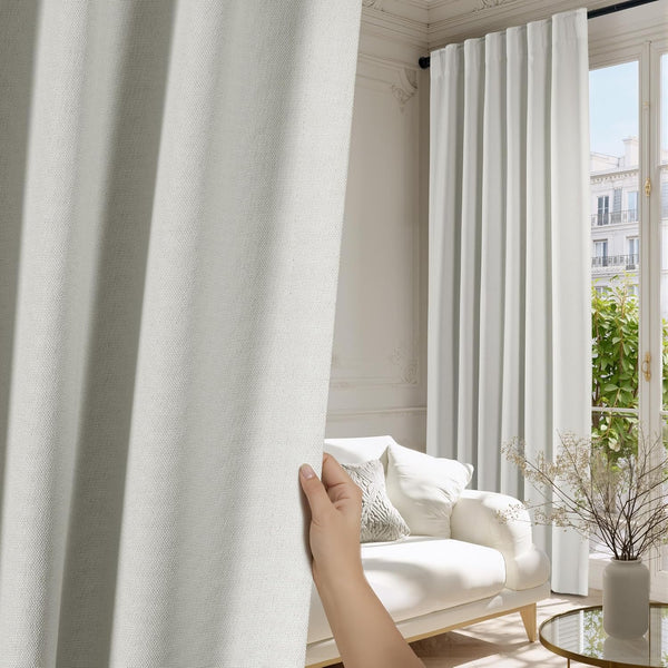 Light grey textured curtain panel with subtle linen-look weave, shown by hand. Elegant living room.