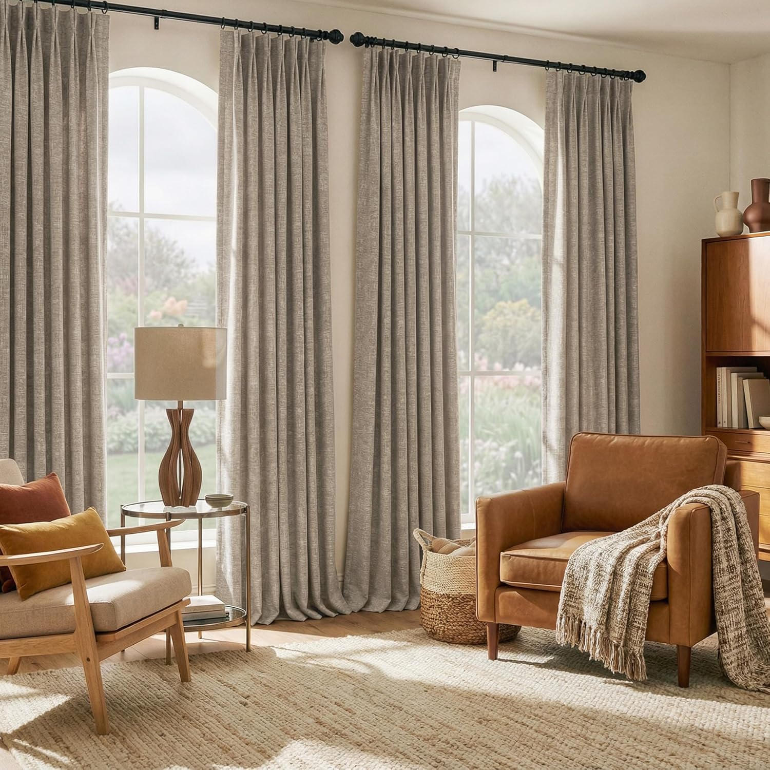 Textured greige pinch pleat curtains hanging from black rods over arched windows in a bright living room.