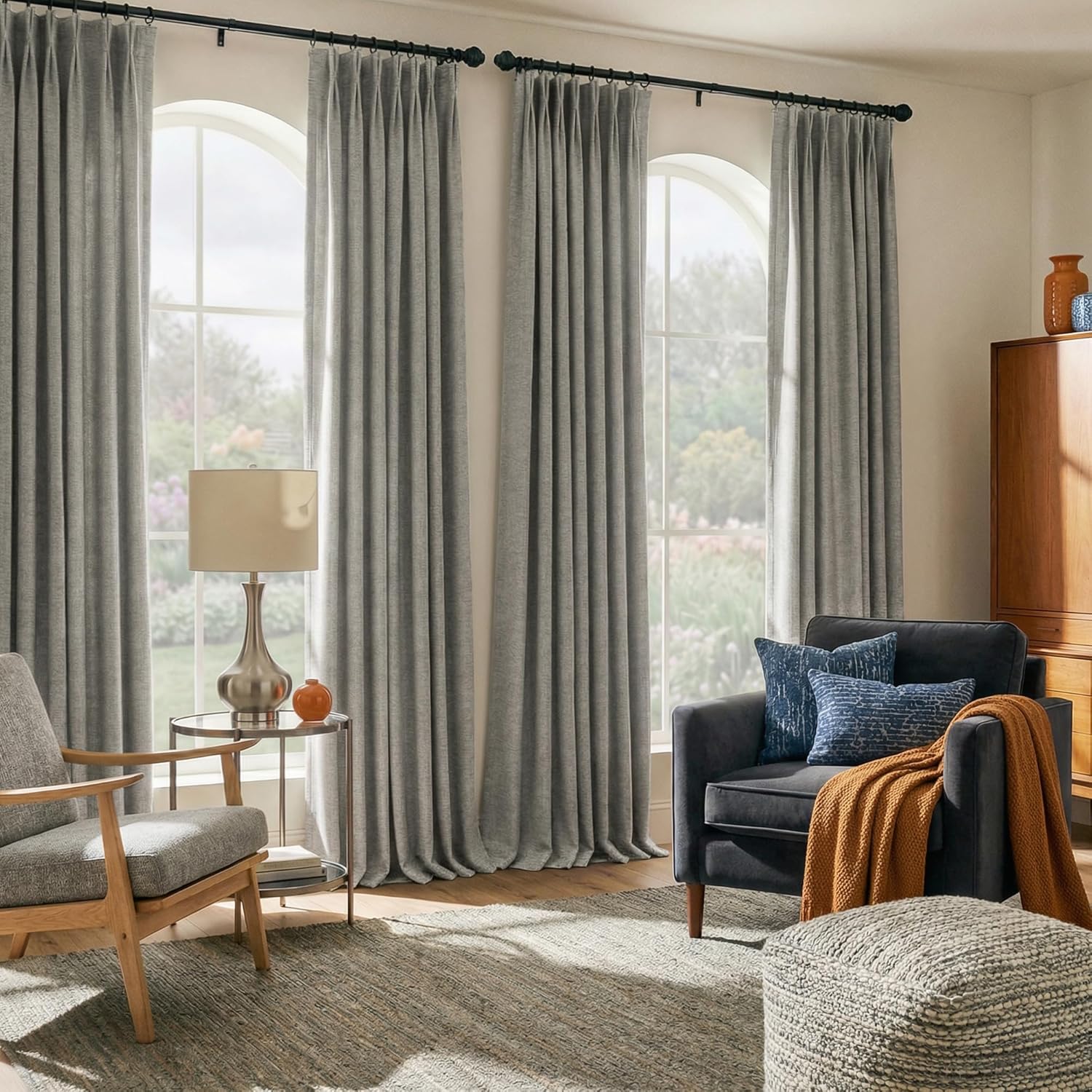 Light grey textured woven curtains with pleats, hanging on black rods over tall arched windows in a bright living room.