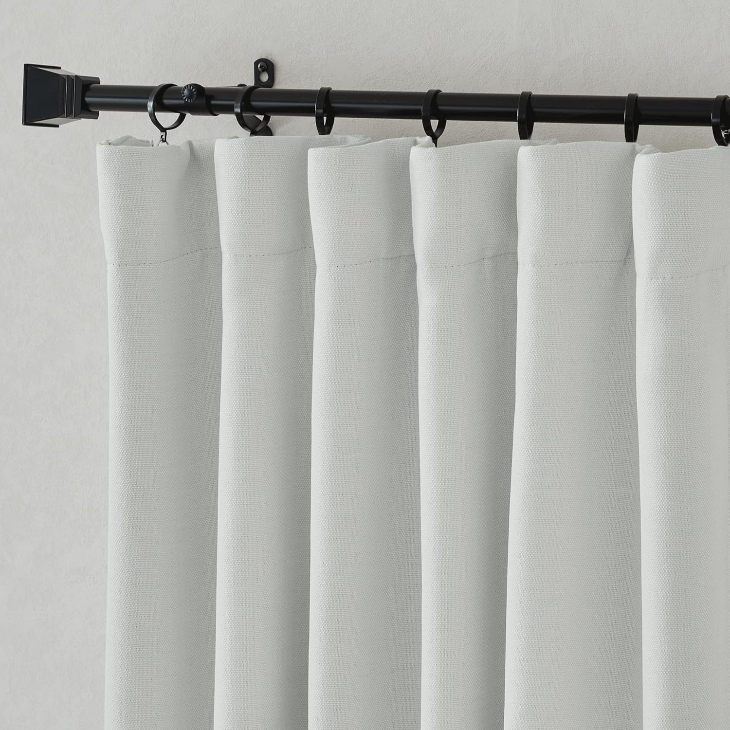 Light grey woven back tab curtain panels hanging on a black rod with rings, showing fabric texture.