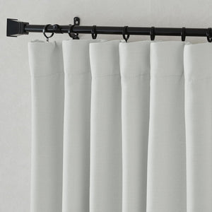 Light grey woven back tab curtain panels hanging on a black rod with rings, showing fabric texture.