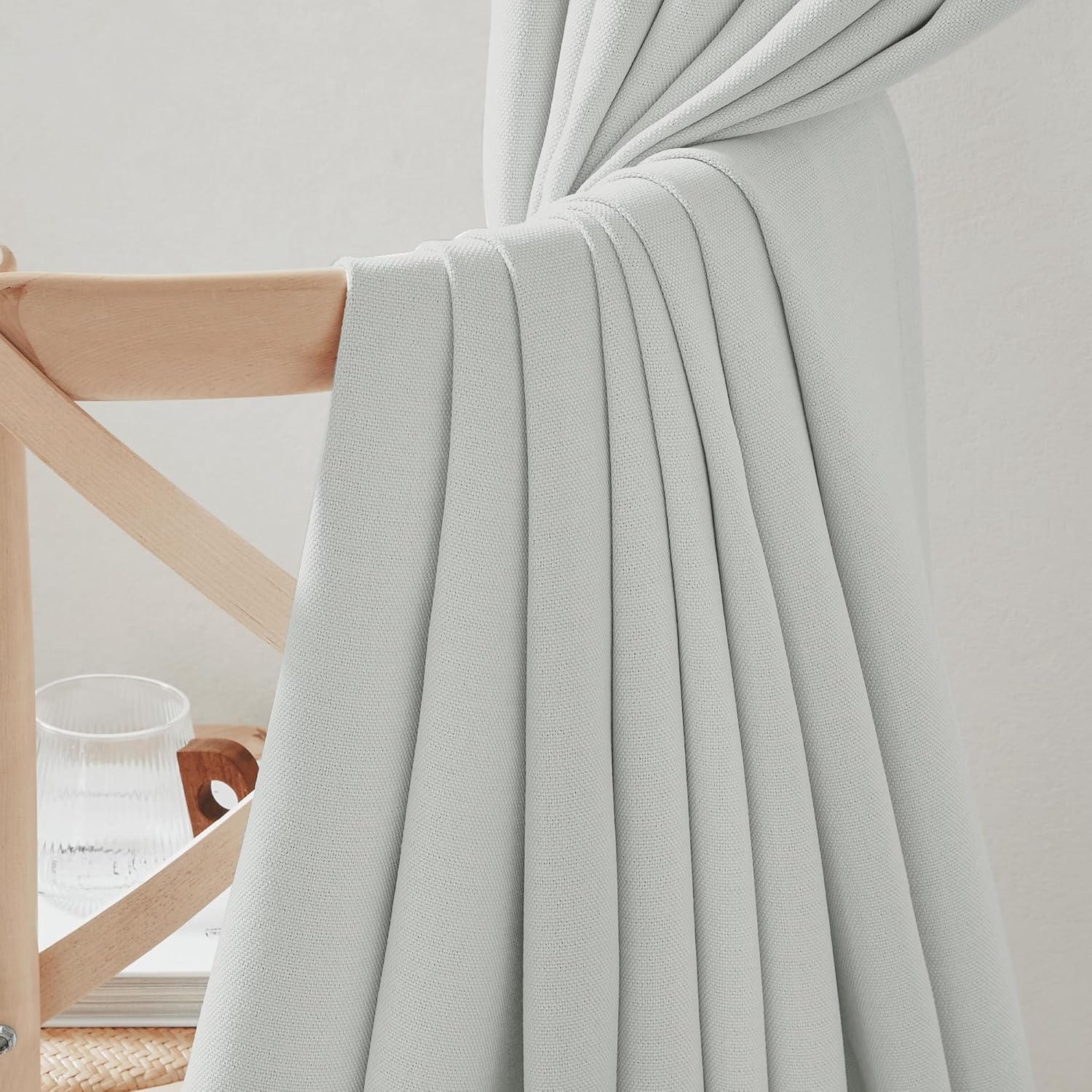 Close-up of light grey textured curtain fabric draped over a wooden chair, highlighting its subtle woven texture and soft folds.