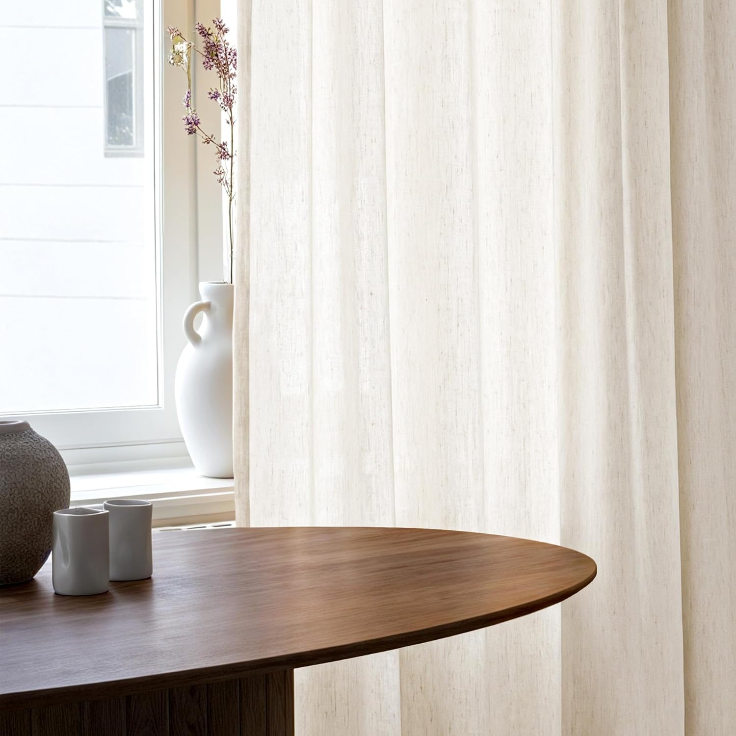 Cream textured fabric vertical panel blinds filtering light, seen next to a wooden table.