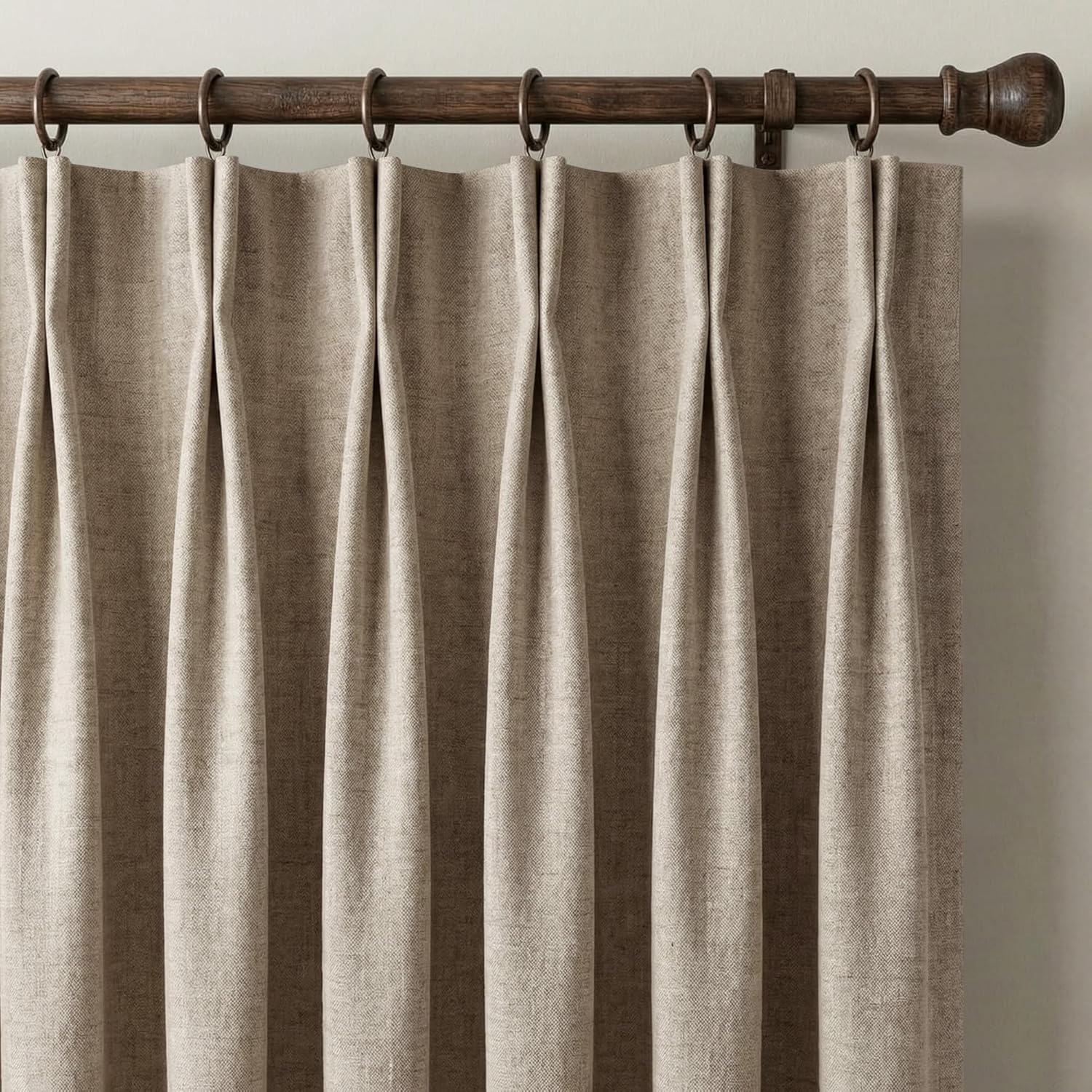 Light natural textured pinch pleat curtains hanging on a dark wood rod with decorative finials.