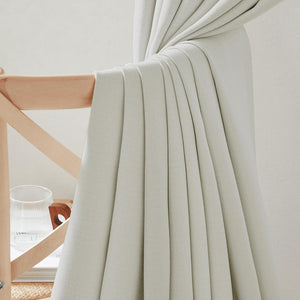 Light sage green textured curtain fabric draped over a wooden chair, showing soft pleats.