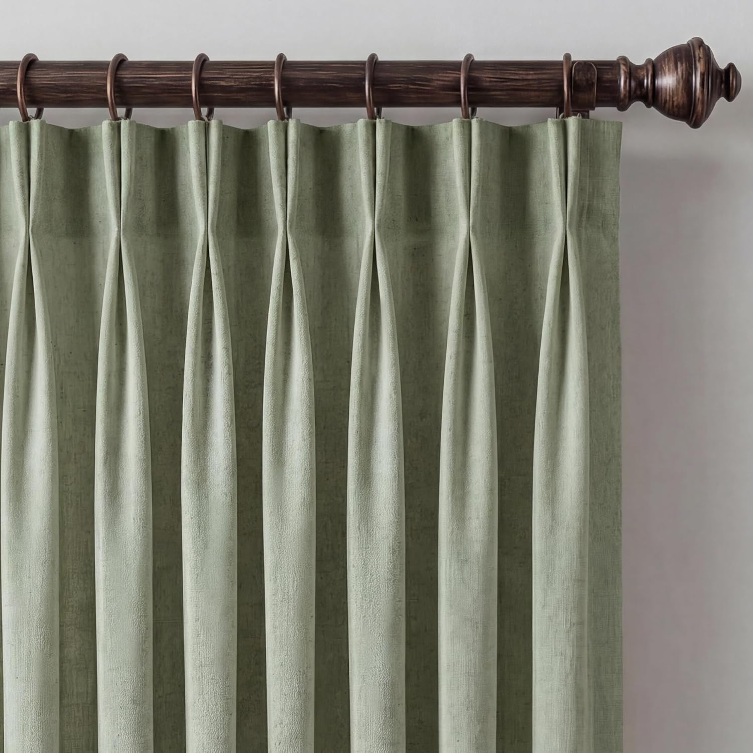 Muted sage green textured curtain with tailored pinch pleats on a dark decorative rod.