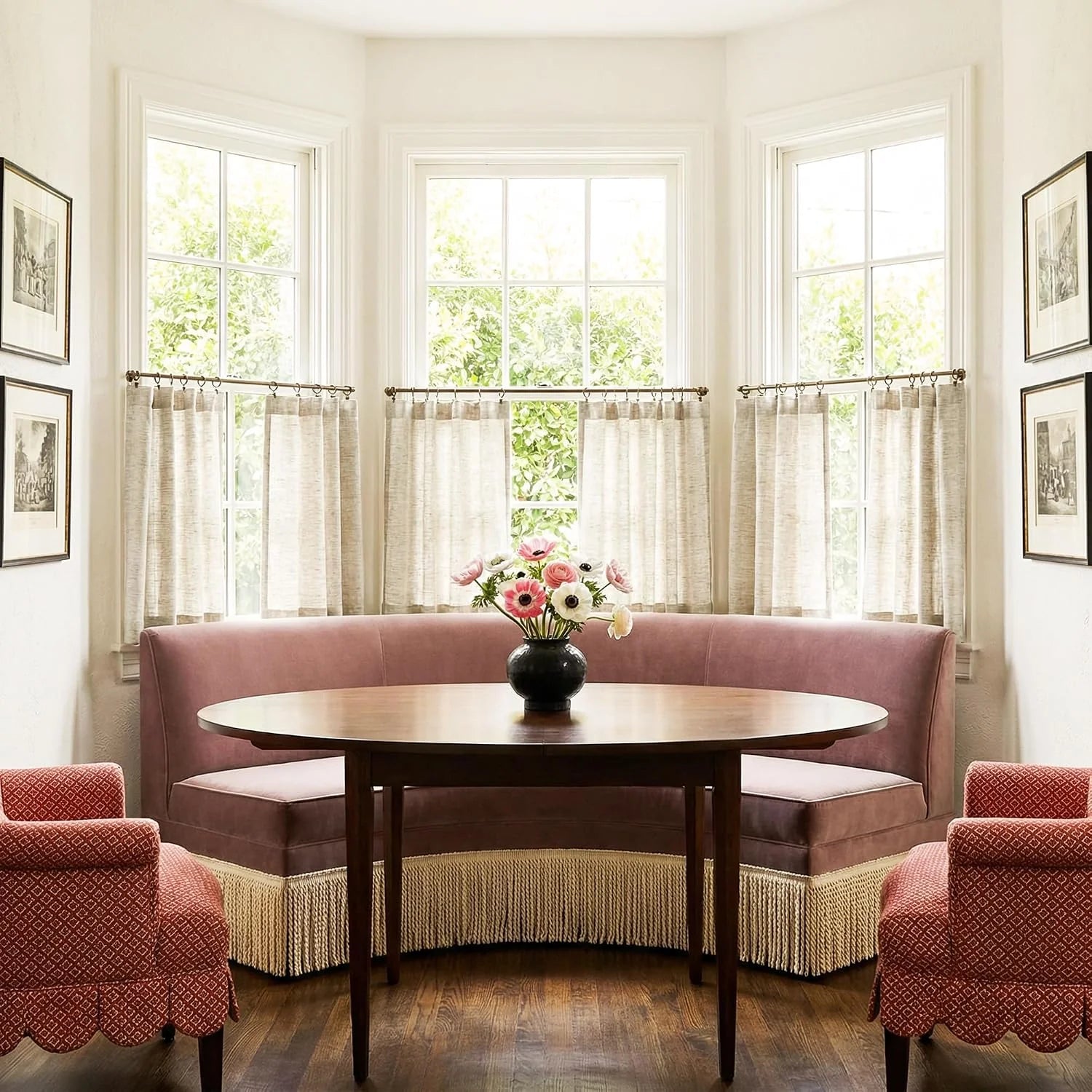 Elegant dining nook with mauve banquette, round wood table, and red patterned chairs beside sunlit bay windows