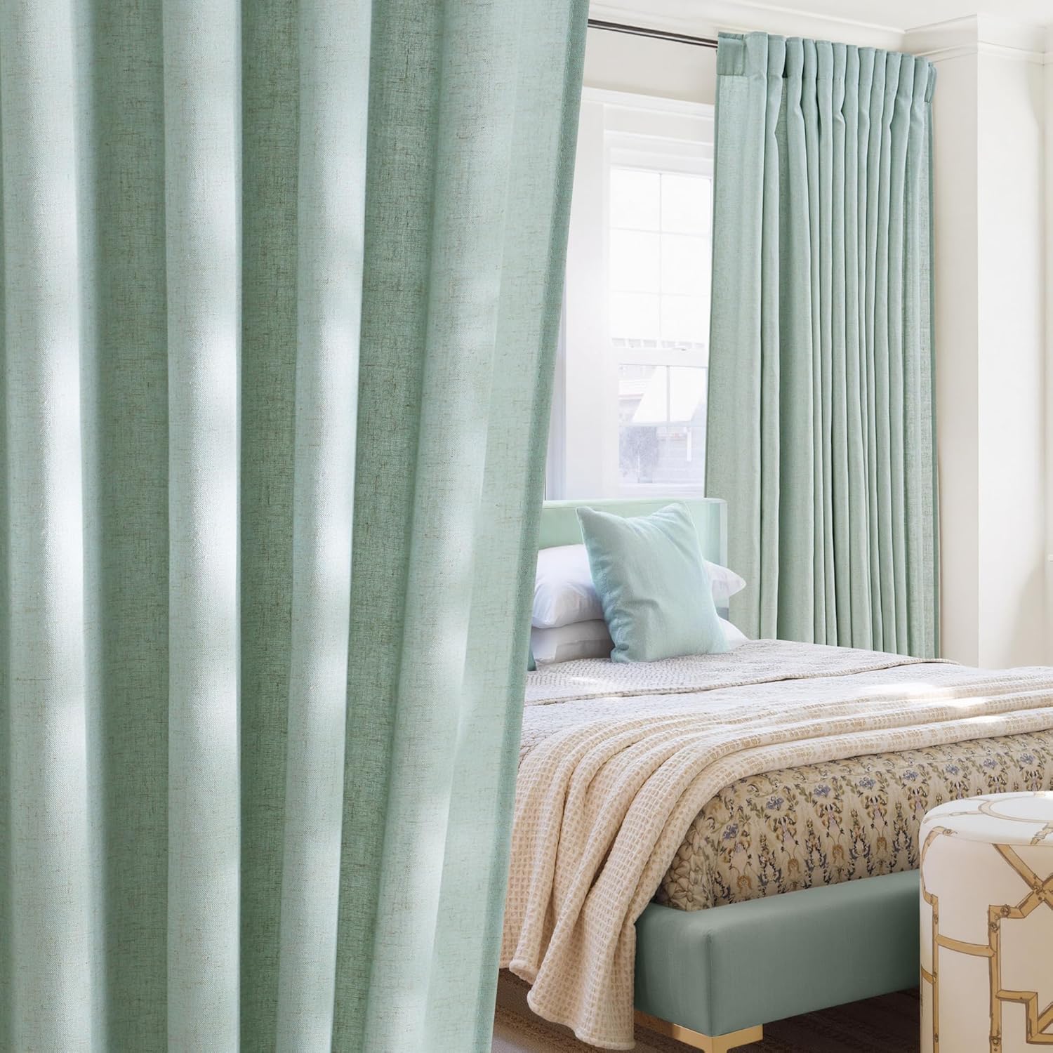 Mint green linen blend pinch pleat curtains hanging elegantly in a bright bedroom, framing a window above a bed.