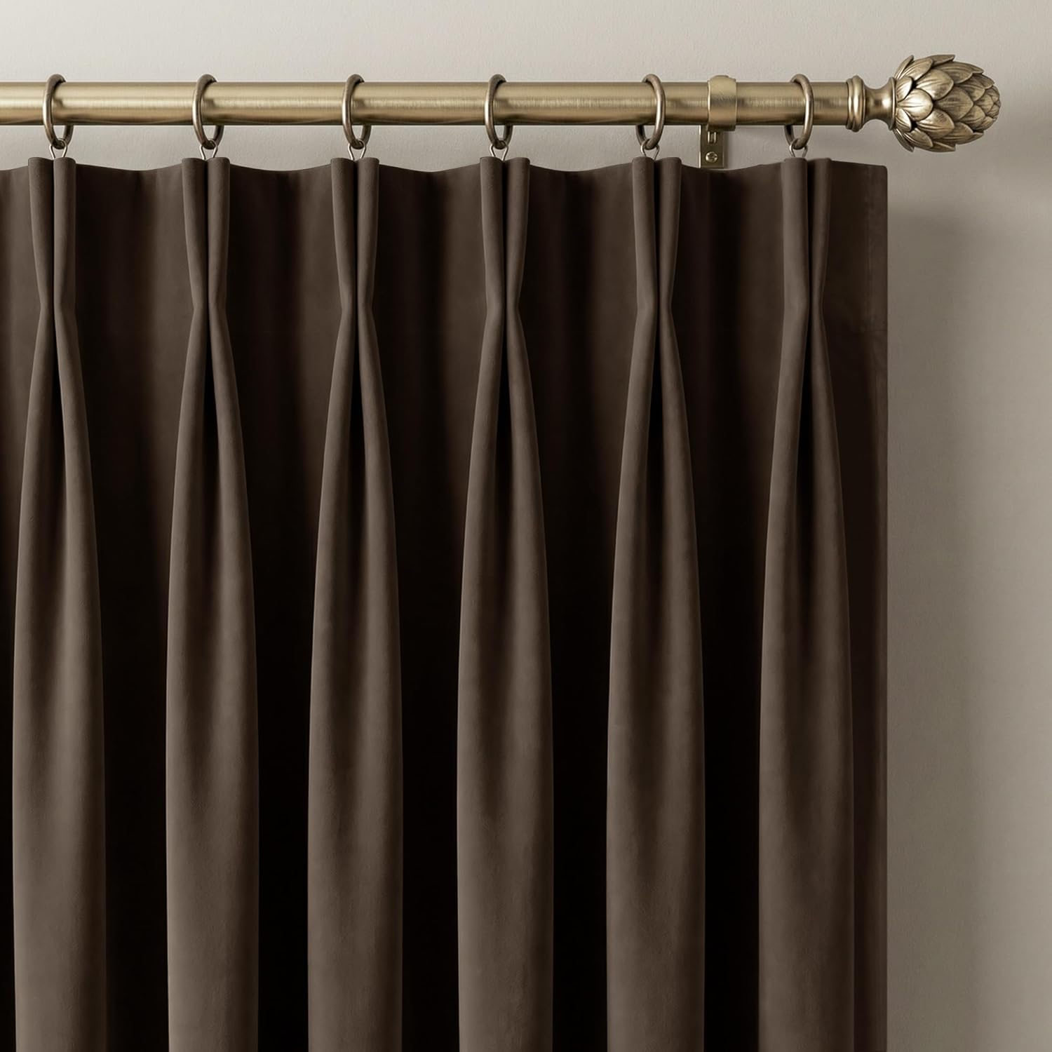Mocha velvet pinch pleat curtains hanging from a brass rod with an ornate artichoke finial.