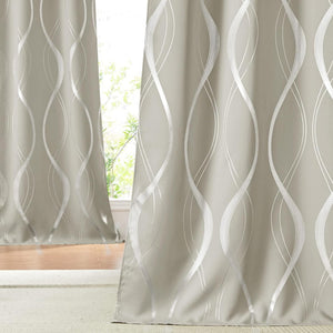 Light greige curtains with a shimmering silver wavy pattern hang in front of a window, resting on a light beige rug.