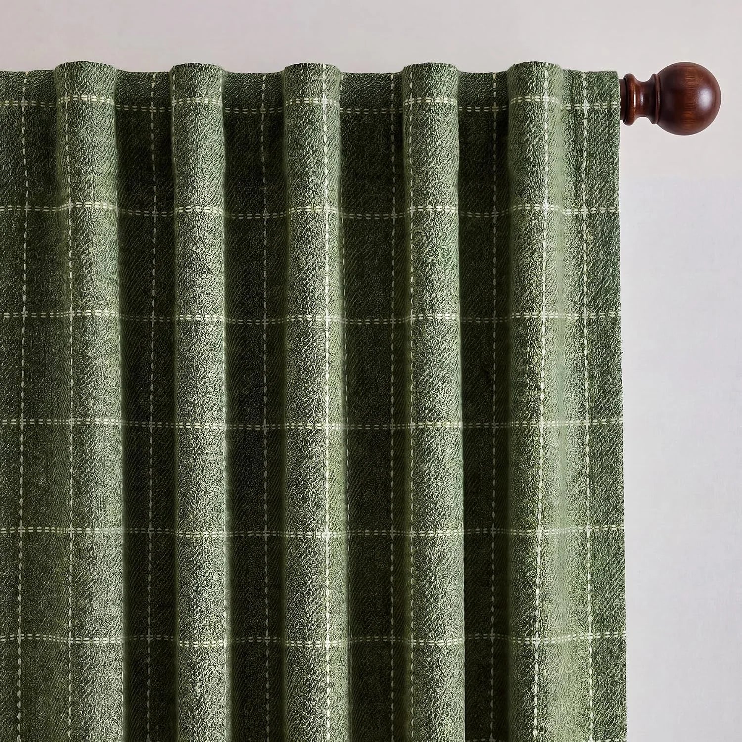 Textured moss green plaid curtain hanging from a dark wood rod with decorative finial.