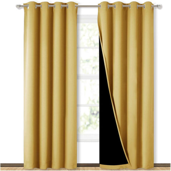Two mustard gold blackout curtain panels with grommet tops on a rod. One panel reveals its black lining.