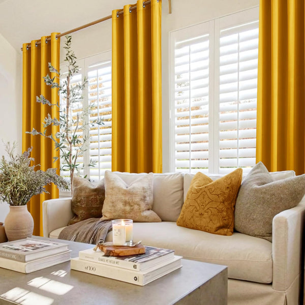 Mustard yellow grommet top curtains hanging in a bright living room, adding a pop of color to the window with white shutters.