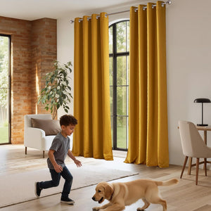 Rich mustard yellow velvet grommet top curtains draped on a silver rod in a bright, modern living room.