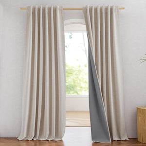 Light beige linen blend back tab blackout curtains with dark grey lining hang on a wooden rod.