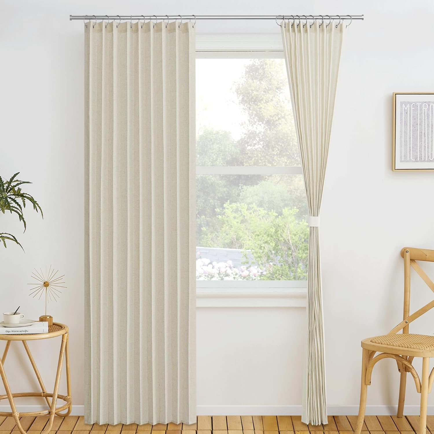 Natural beige linen ripple fold drapes on a window, one panel tied back revealing a view of trees.