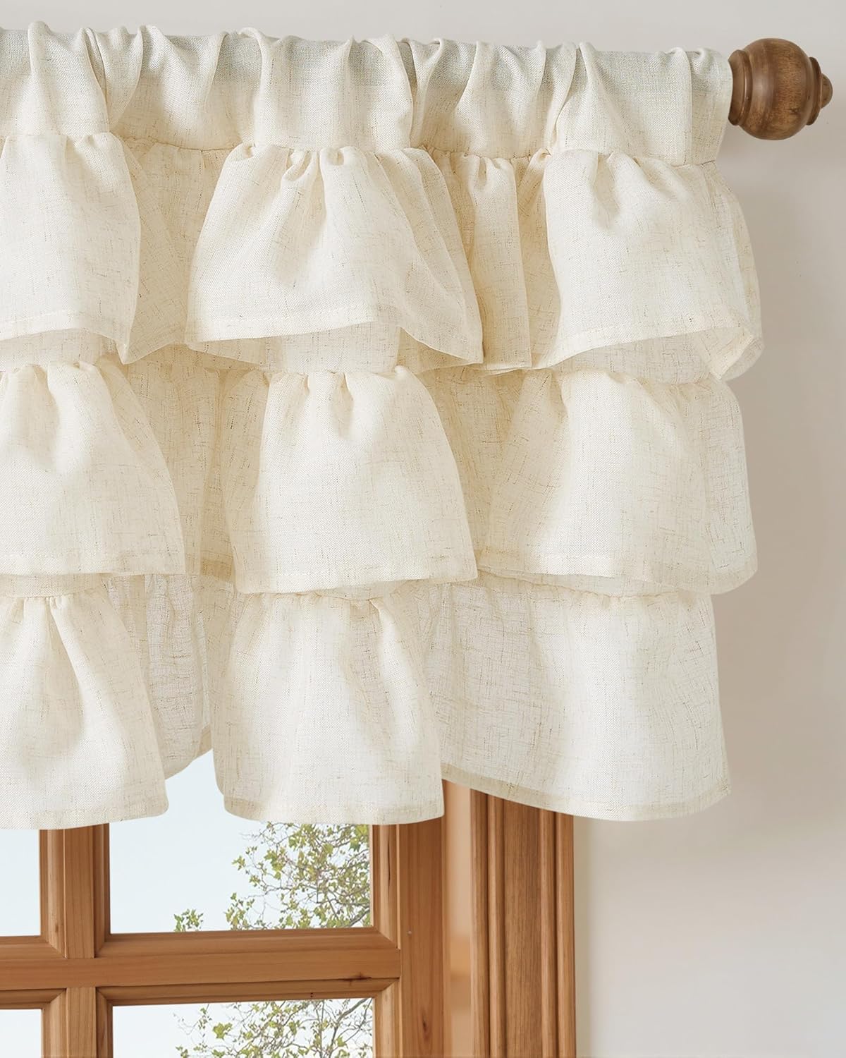 Natural cream linen tiered ruffle valance with slub texture hanging on a wooden rod above a window.